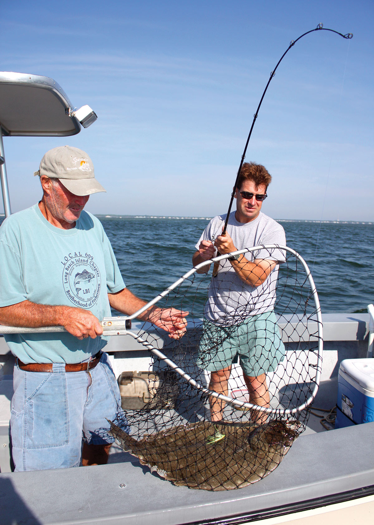 Two men on a boat with a fishing rod and net catching a fluke fish