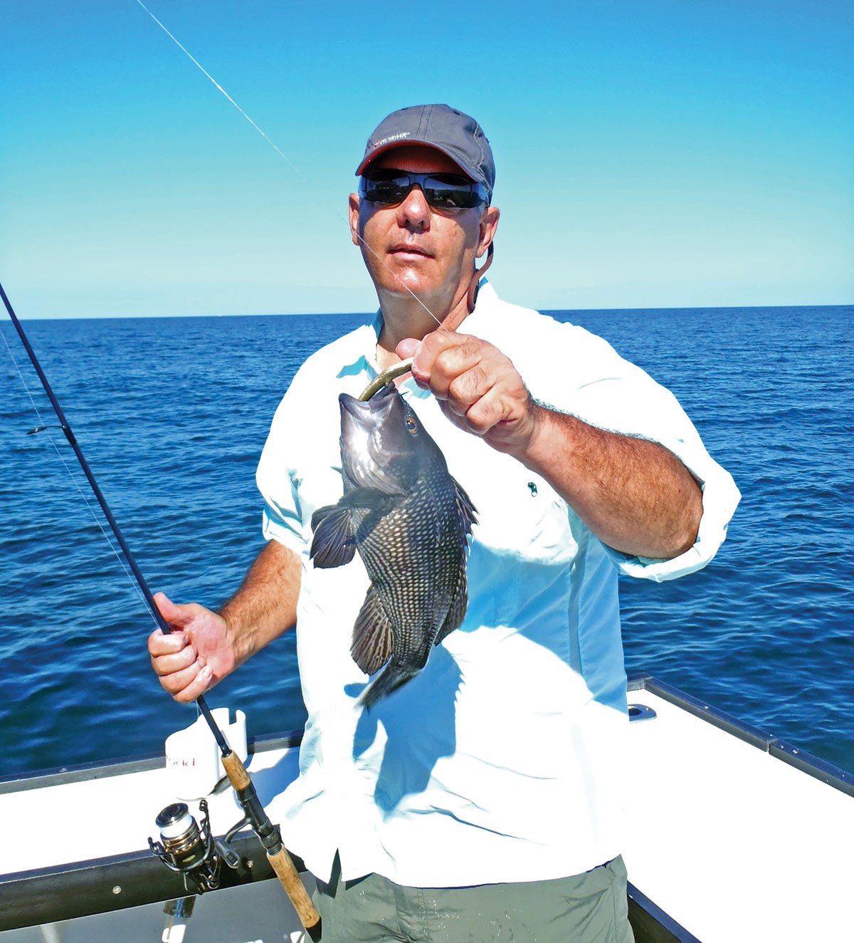 man in white shirt holding a fishing rod and black fish in a boat