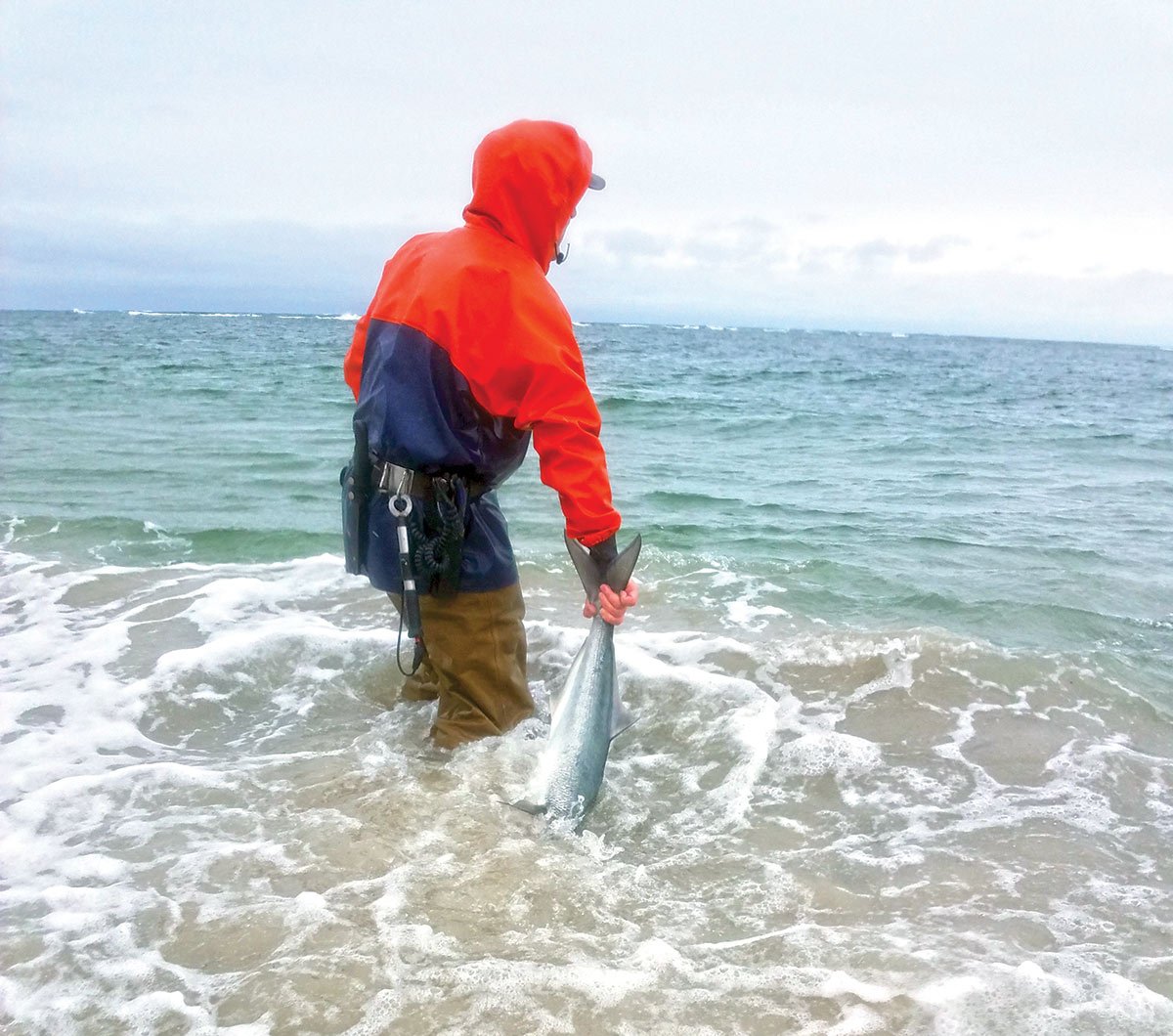 man in red hood holding a fish in the shore