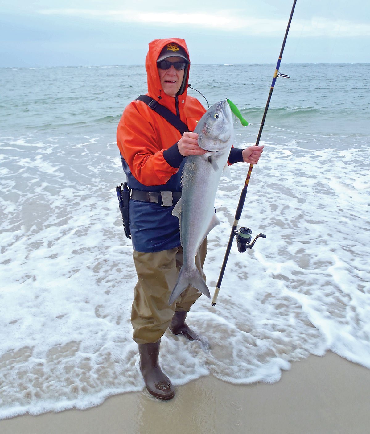 man in red hood holding a fish up and a fishing rod