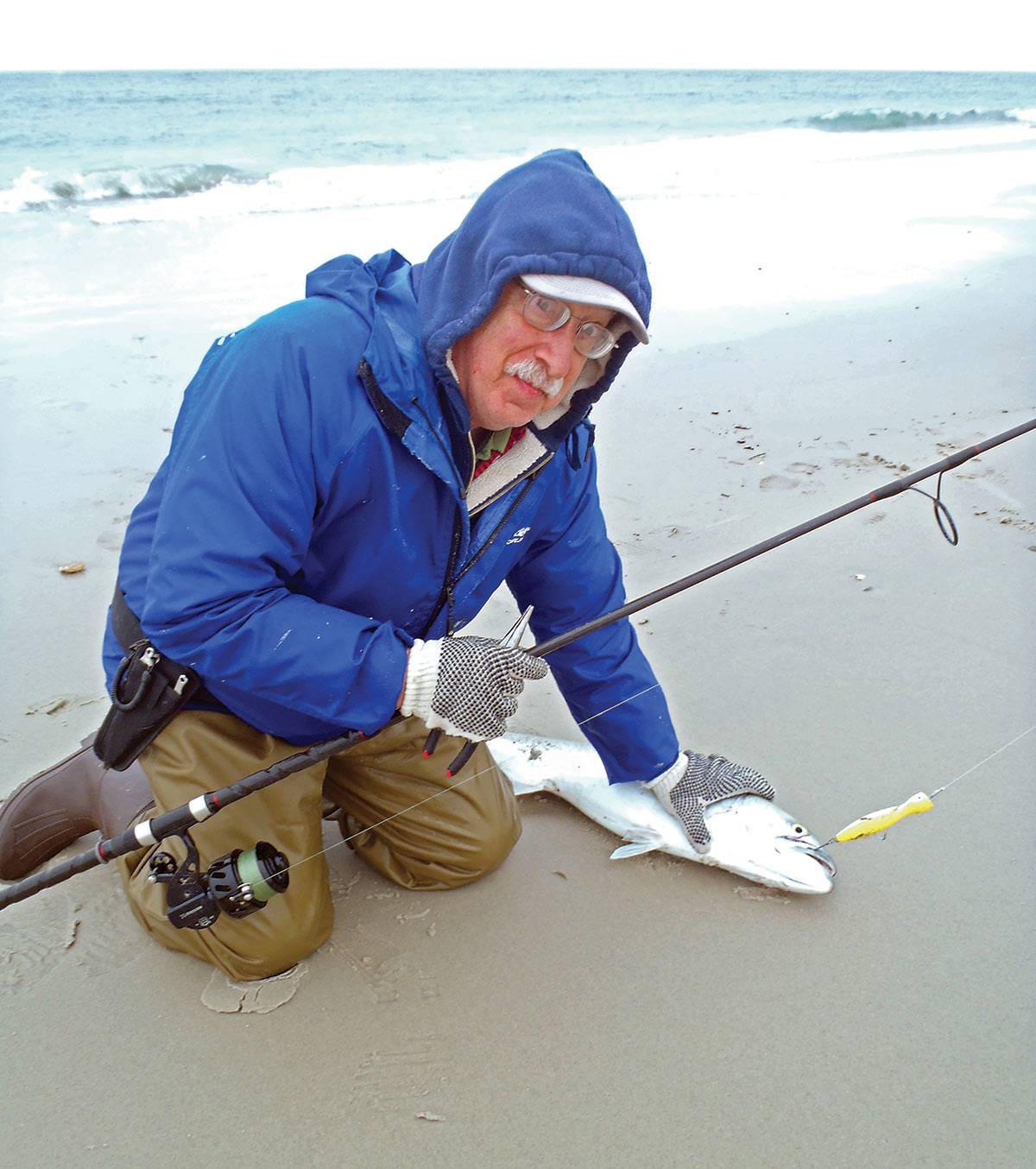 man in blue sweater holding down a fish on the sand