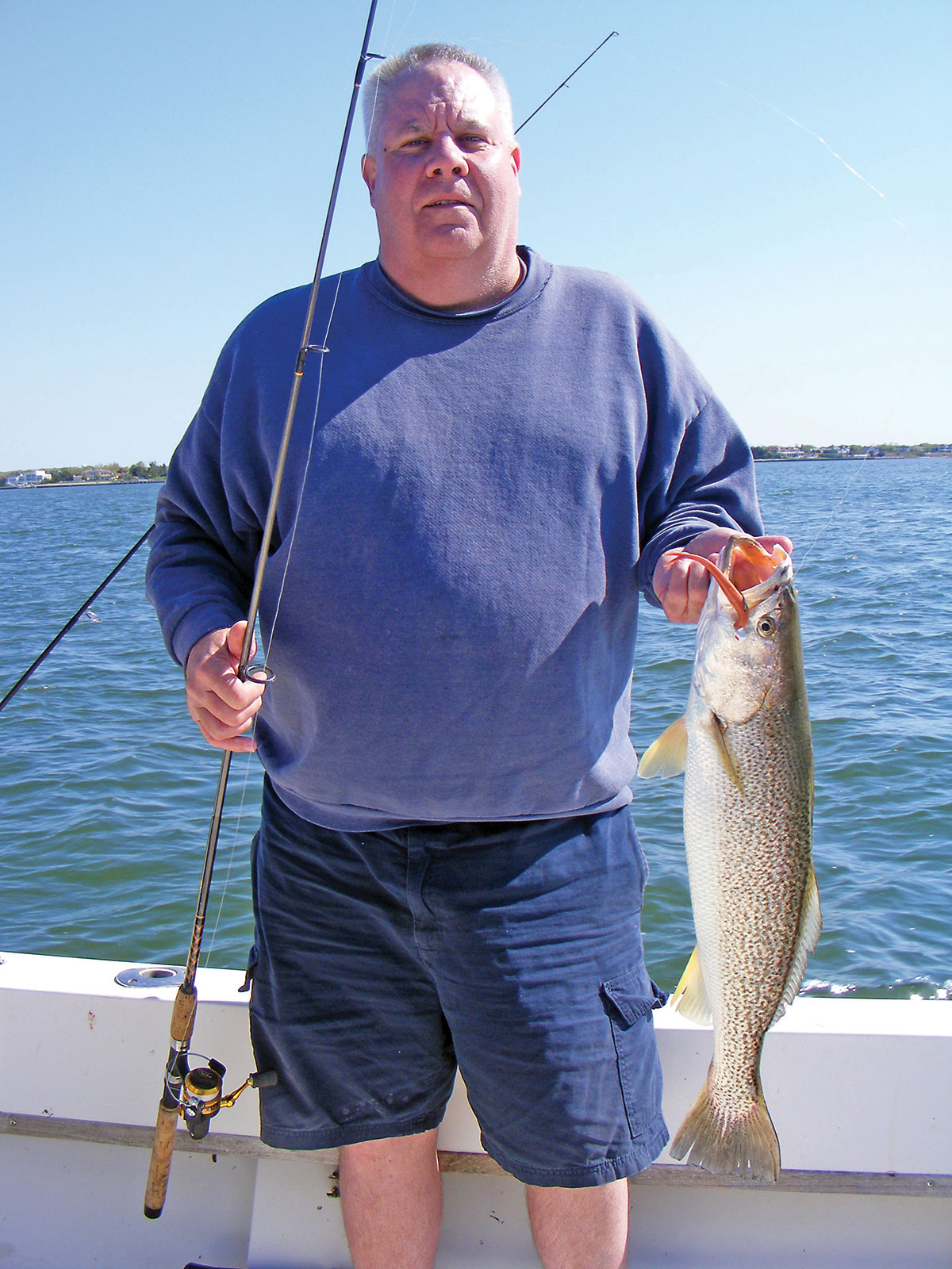 Man on a boat holding the fish he caught and a fishing rod
