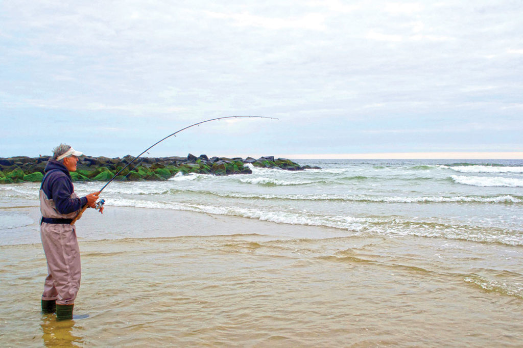 Man in jumpsuit standing in the shore holding a fishing rod
