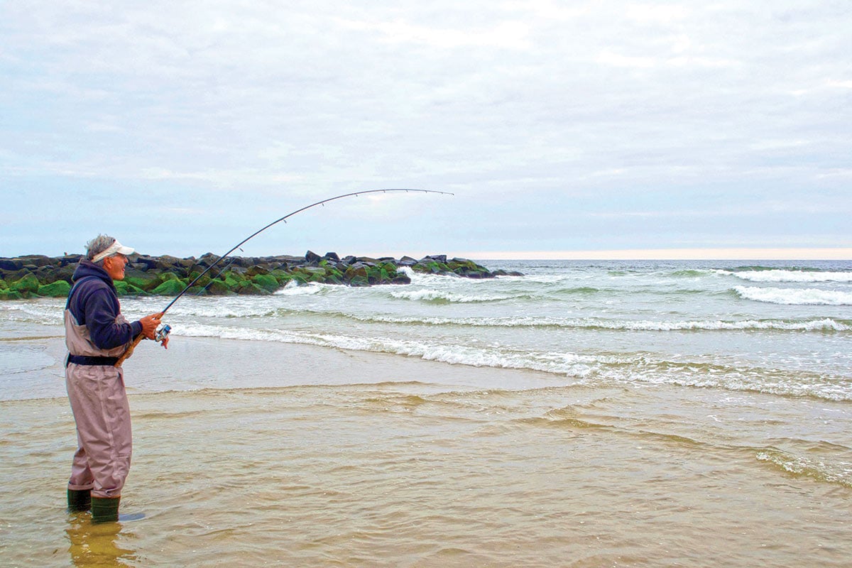 Man in jumpsuit standing in the shore holding a fishing rod