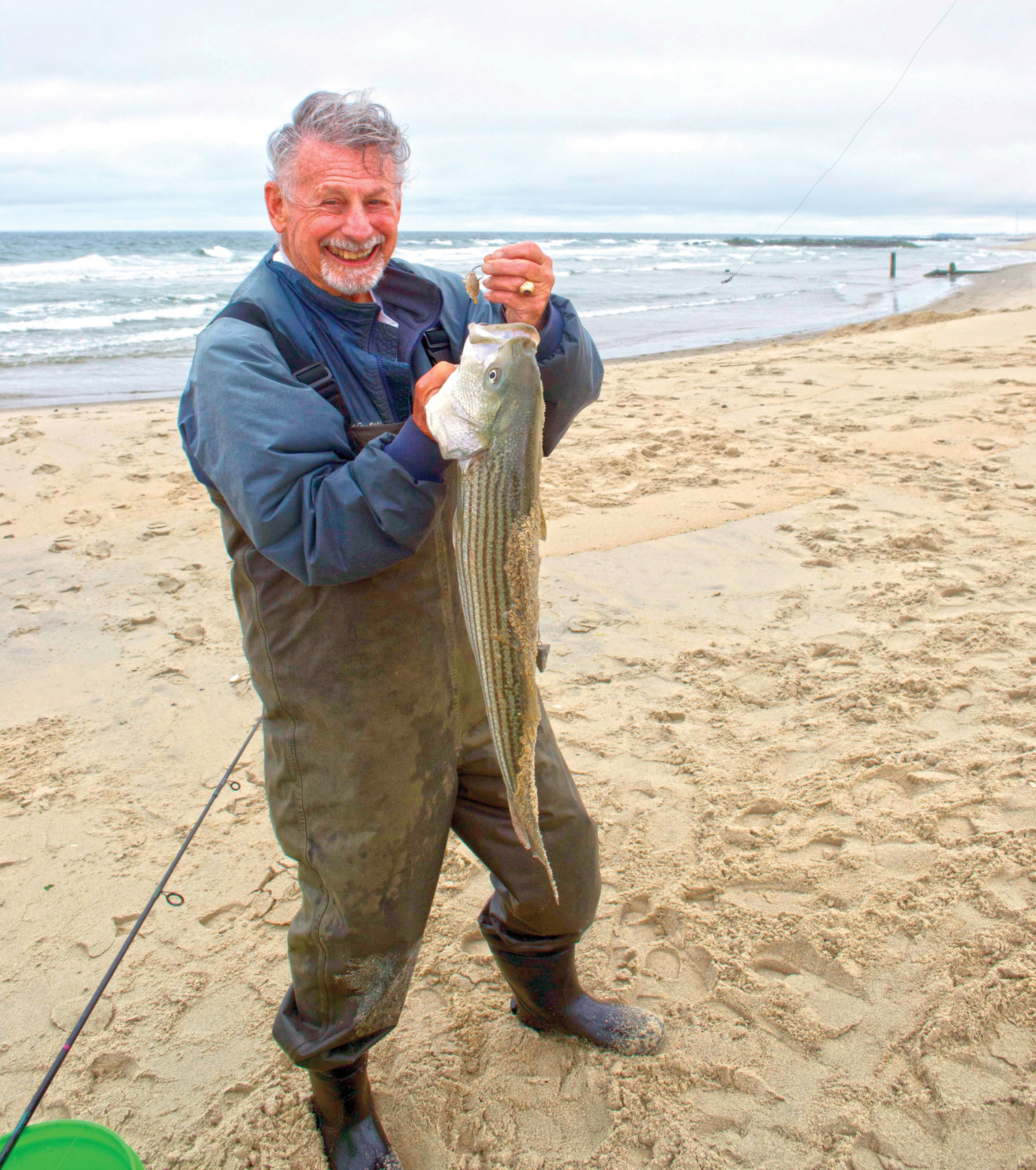 Man in jumpsuit in the sand holding the fish he caught