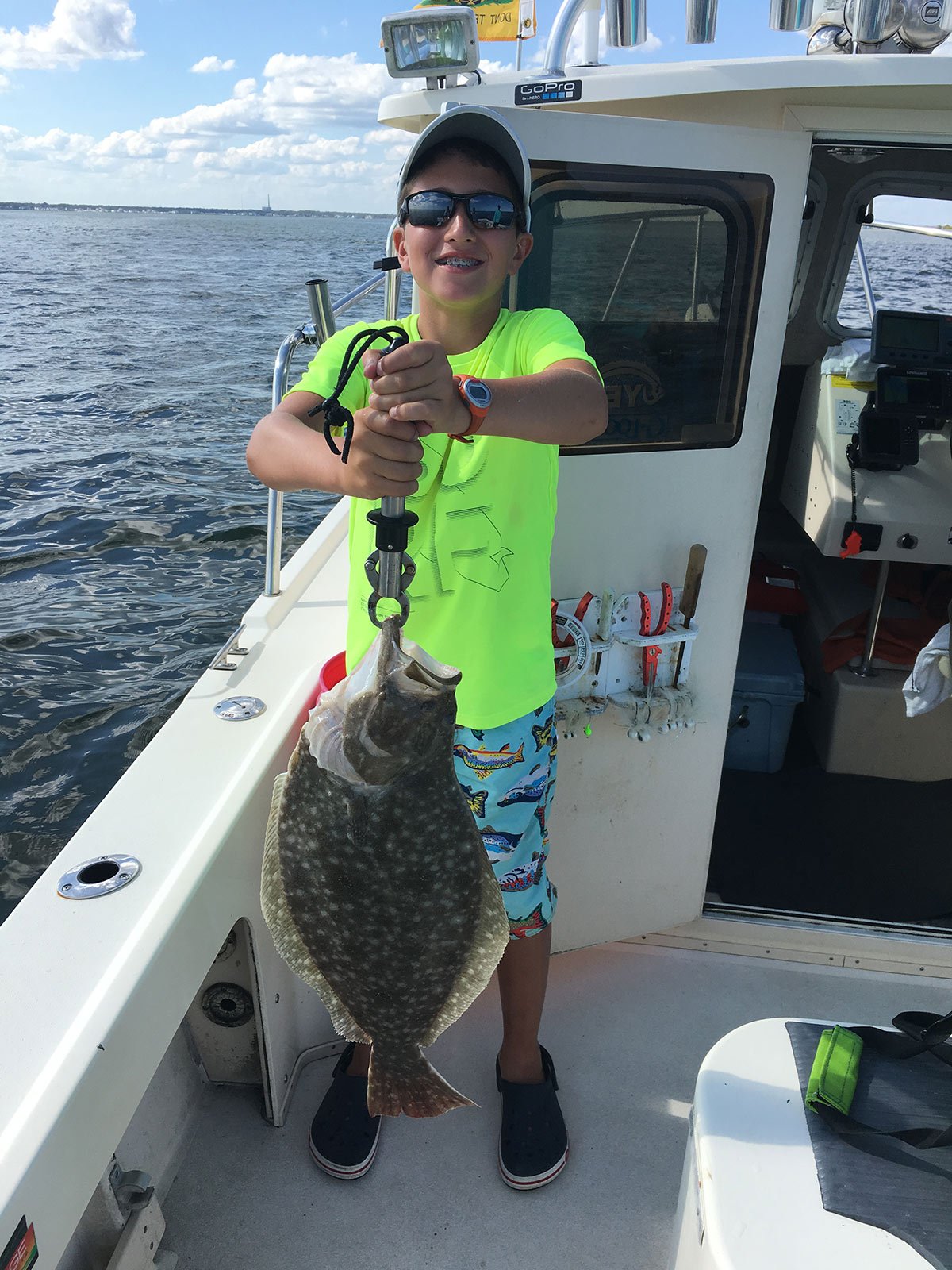 boy in neon shirt showing off the fluke fish he caught