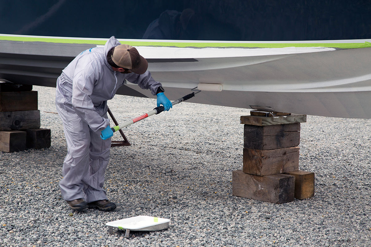 man in jumpsuit painting the bottom of a boat with white paint