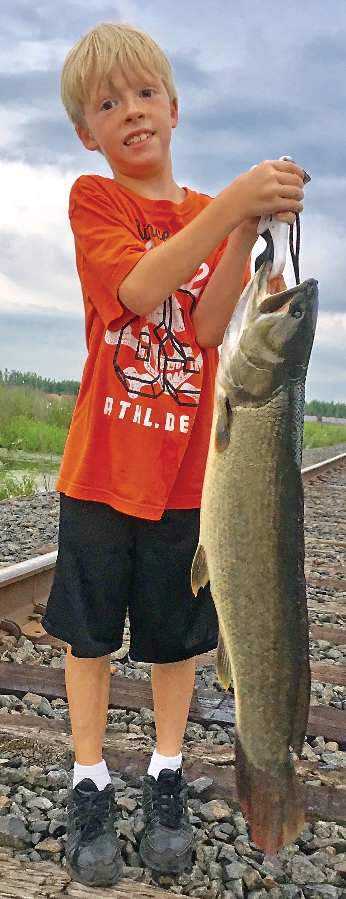 Boy in train tracks holding up a bowfin fish