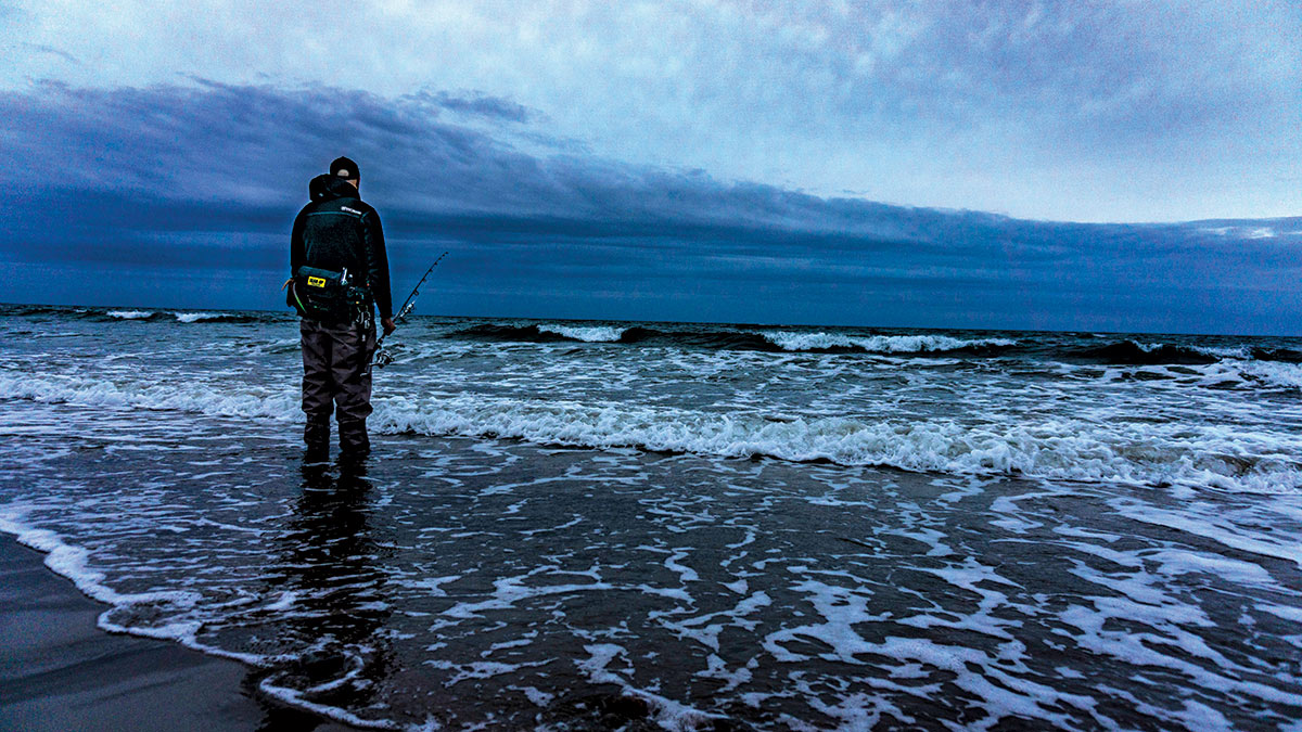 Man standing in the shore holding fishing rod