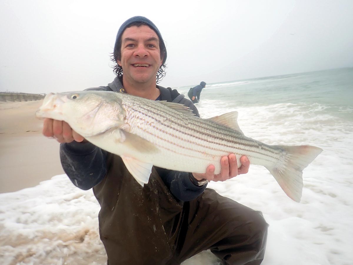Man showing off a striped bass he caught during an overcast day