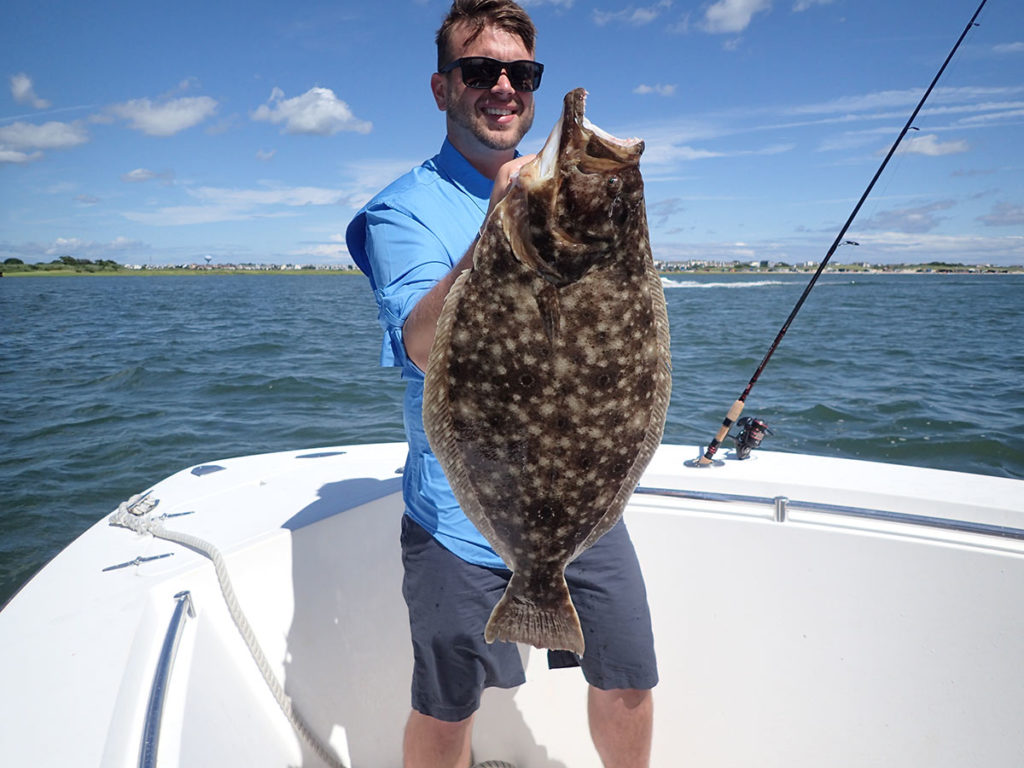 A man in blue shirt shows off the big fluke he caught