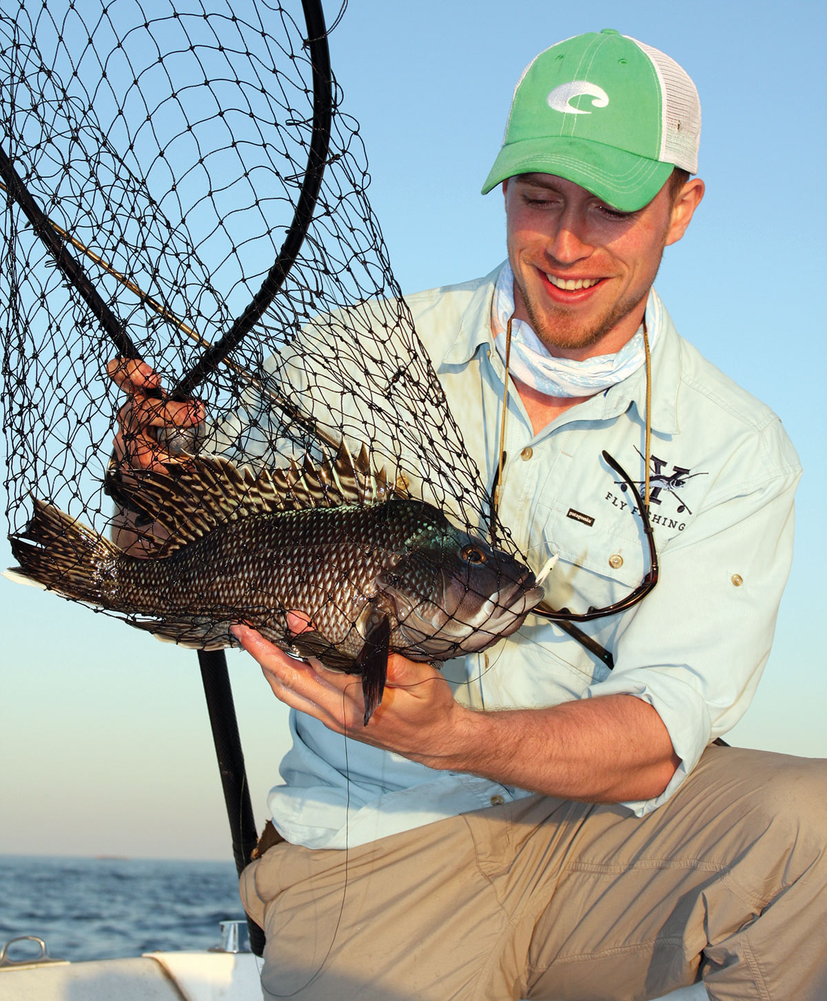 Man in cap showing off black sea bass inside fish net