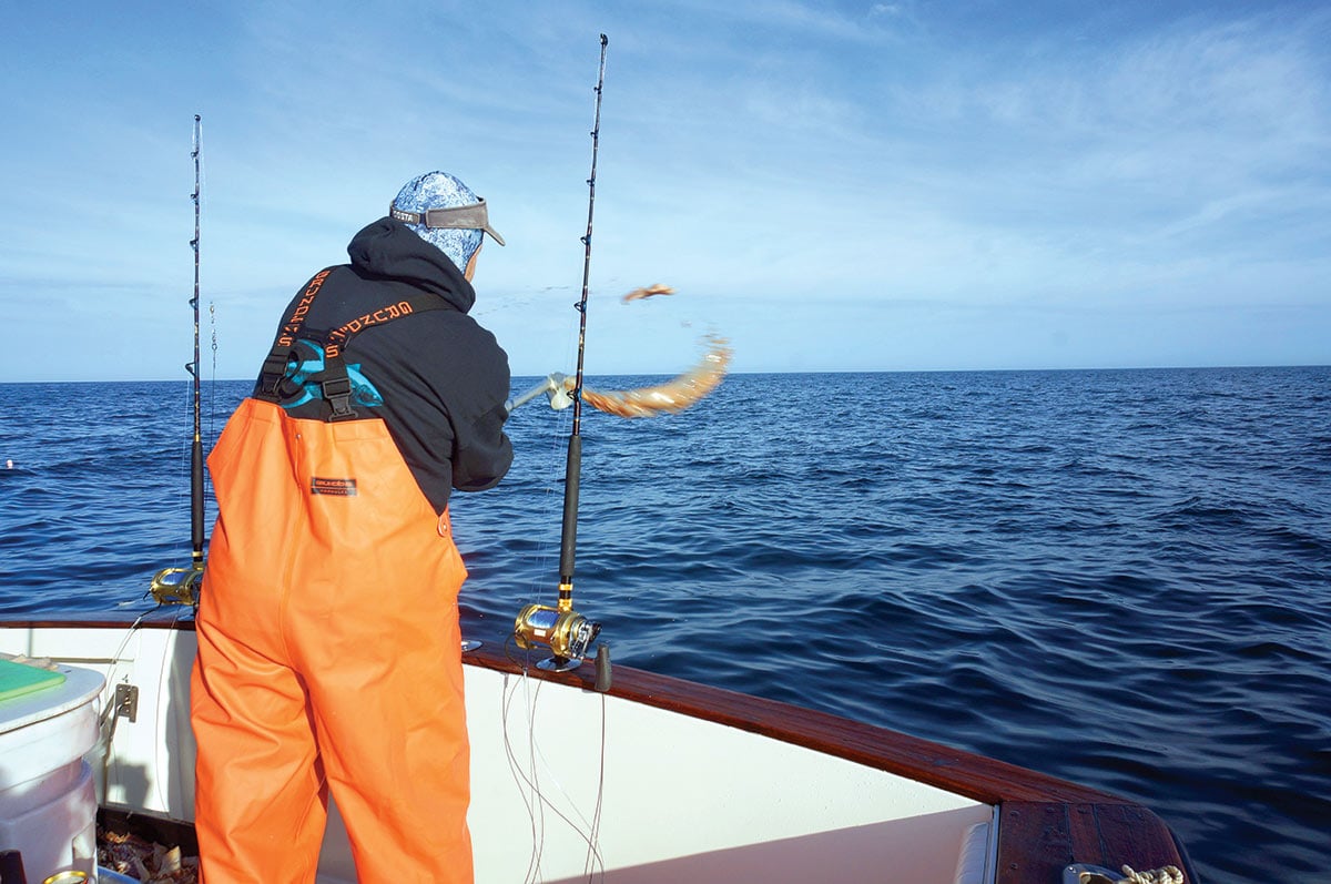 Man in orange jumpsuit throwing bait into the water to lure mako sharks